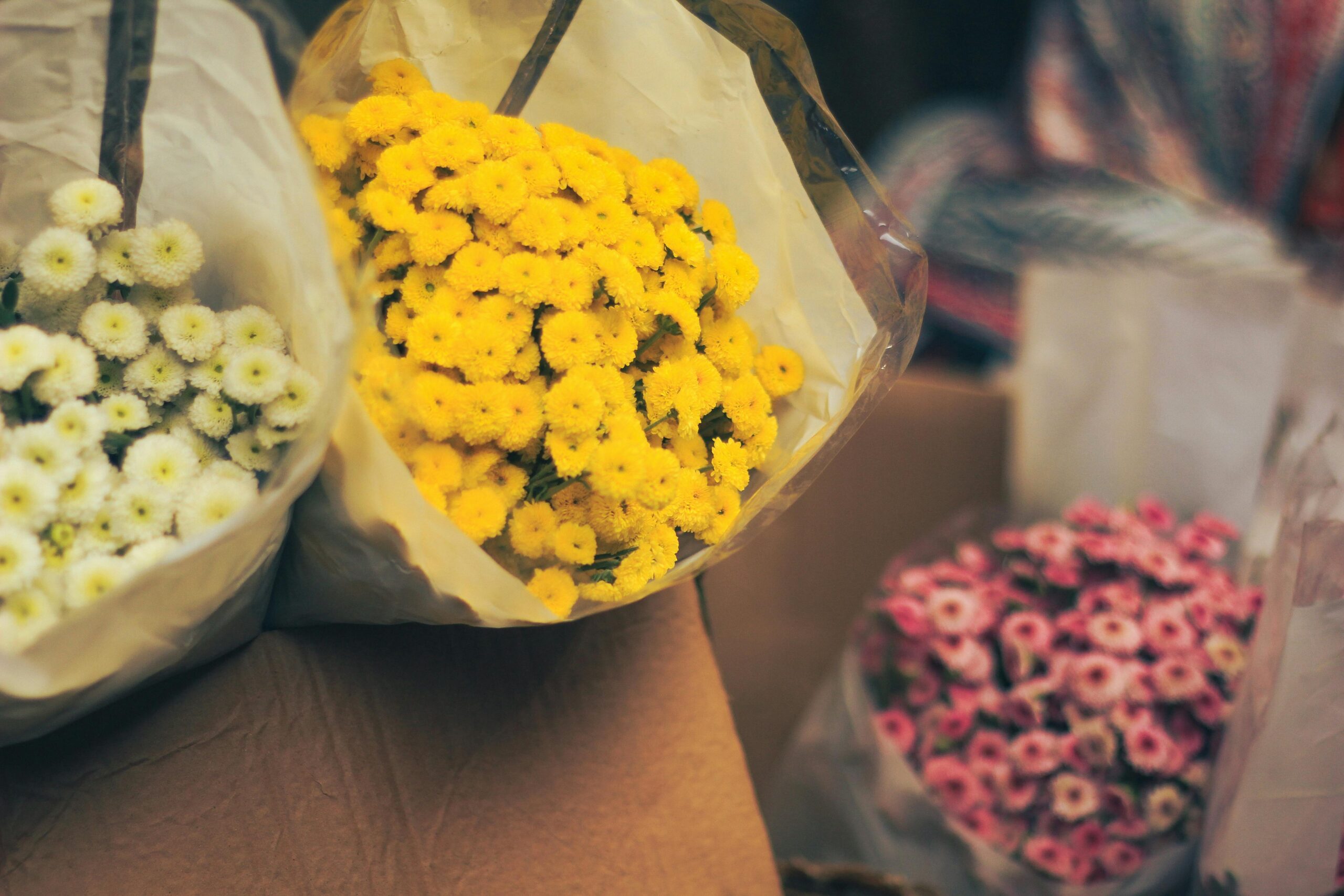 Colorful bouquets of pink, yellow, and white flowers wrapped in a Dhaka market setting.